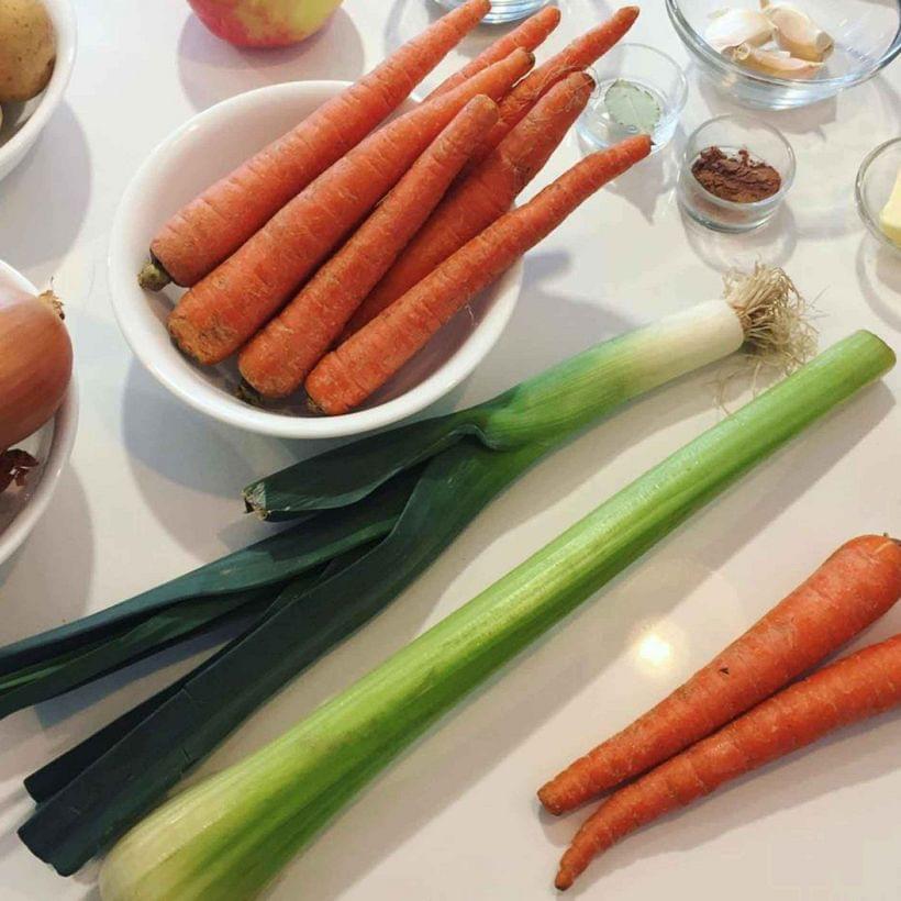 Mise en place; tiny bowls of various spices and herbs, a large bowl of whole carrots, a leek, and a celery stalk.