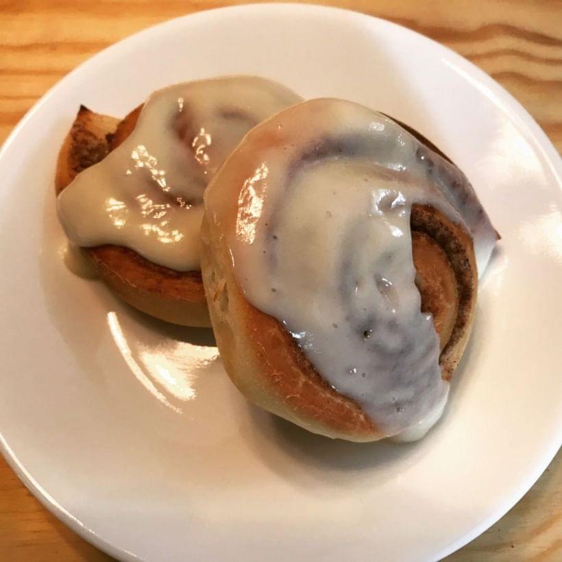 Two spiraled cinnamon buns on a small plate, covered in icing.