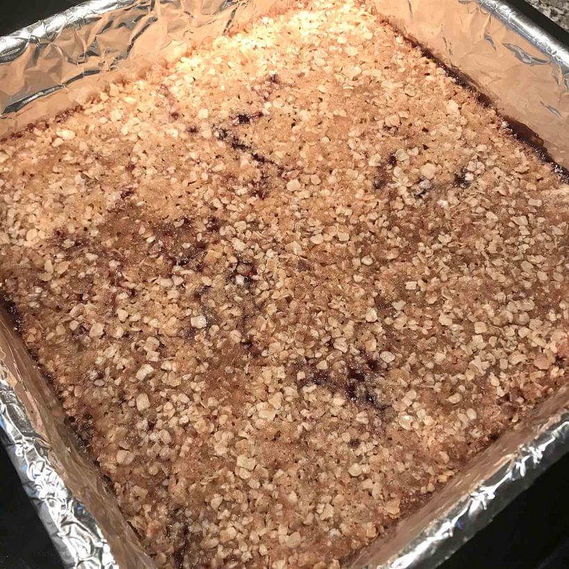 An uncut tray of raspberry bars, with the filling just showing through the topping in places.