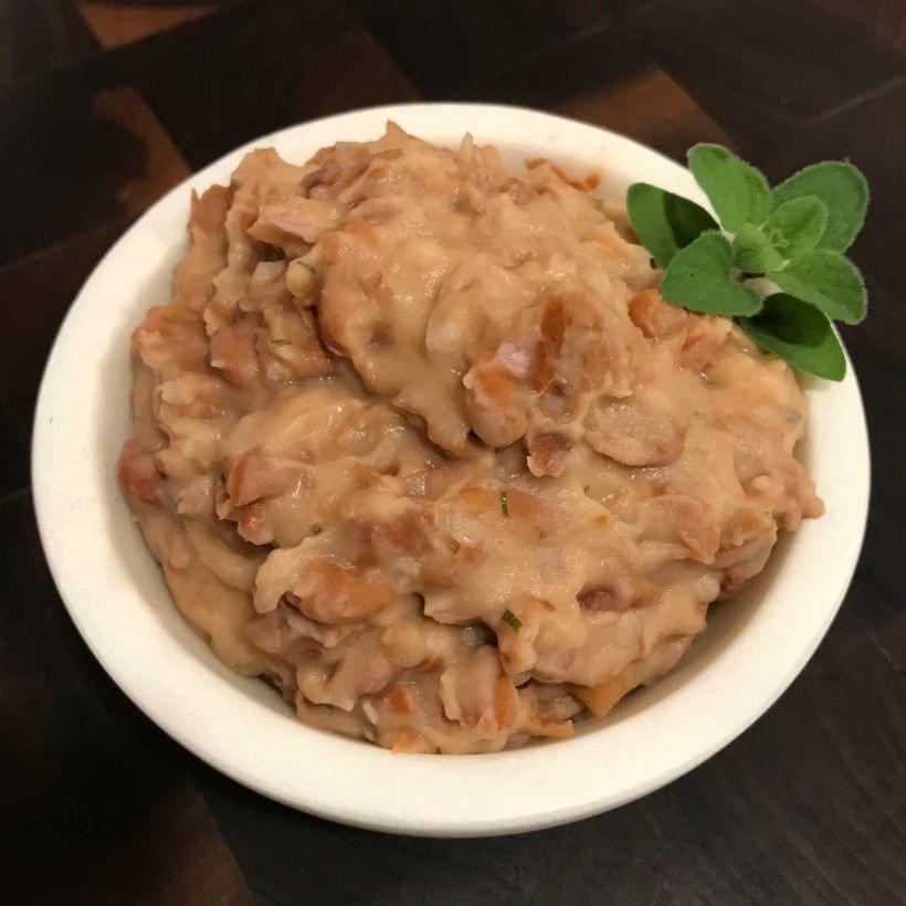 A bowl of partially-mashed refried beans, with a sprig of oregano as garnish.