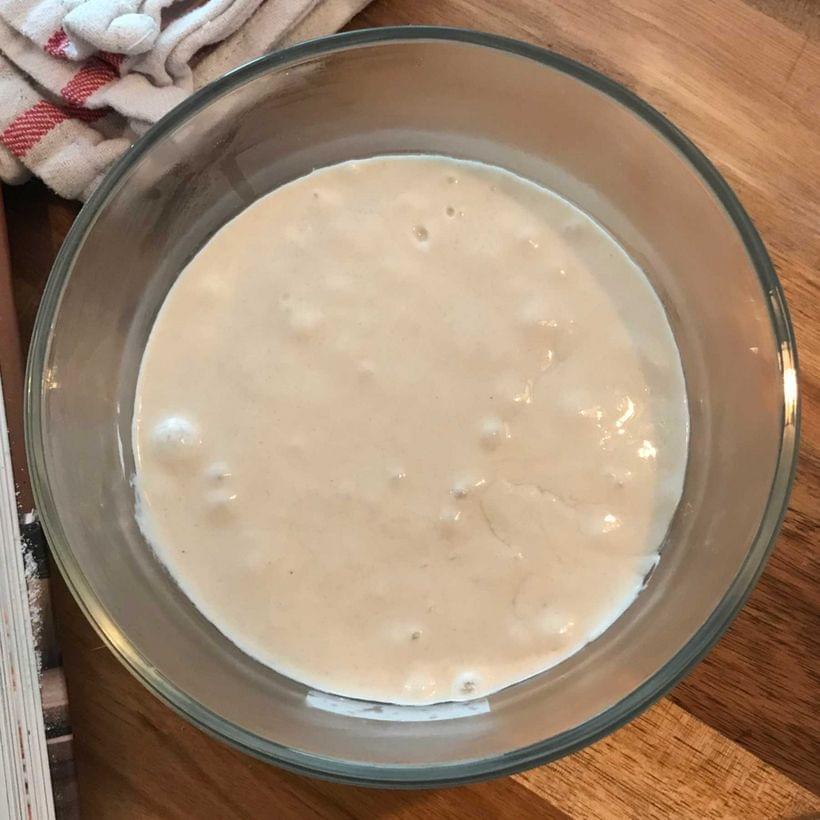 A clear glass bowl containing a wet, bubbling dough.